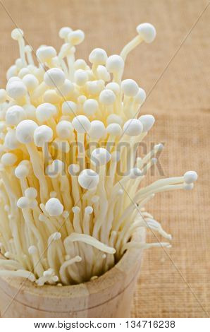 Fresh Enoki mushroom in wooden cup on sack background.