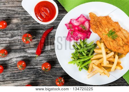 Bread Crumb Coated fried pork chop with french fries fried green bean and salad with dill and cabbage marinated in red wine vinegar and beet juice studio lights close-up view from above