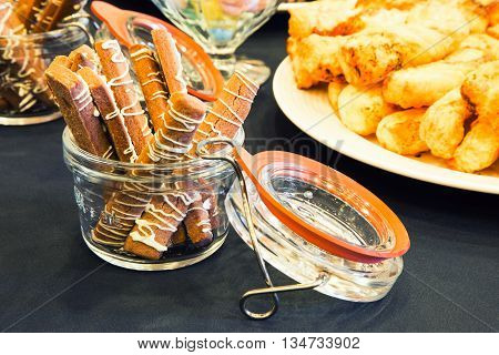 Delicious dessert fingers drizzled with frosting and displayed in a glass jar besides other tasty treats