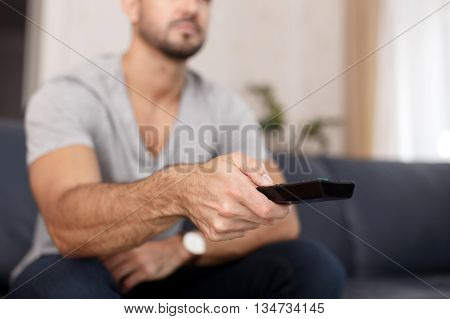 Man chaning TV channel by remote control at home