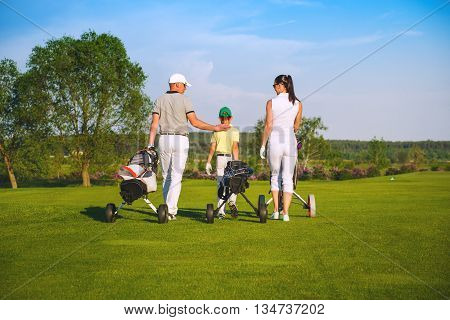 Family golfers plaing golf at sunny day, back view
