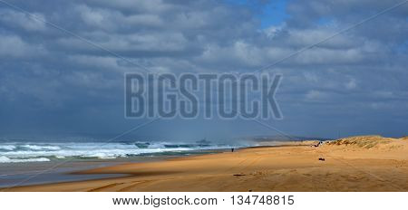 Horizontal landscape of the beach with a fisherman, shipwreck in the background and dramatic clouds (Stockton Beach, NSW, Australia)