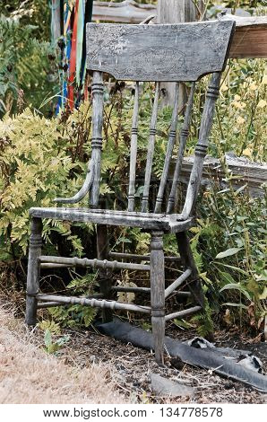 Old wooden rocker sitting in weeds next to a fence.