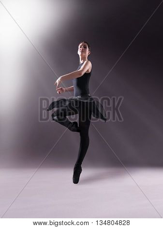 Young ballerina in black outfit posing on toes, studio background.