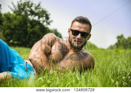 Handsome Muscular Shirtless Hunk Man Outdoor in City Park. Showing Healthy Muscle Body While Looking away, wearing sunglasses