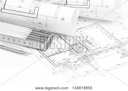 Rolls Of Architectural Blueprints, Folding Rule And Pencil On Floor Plan Background