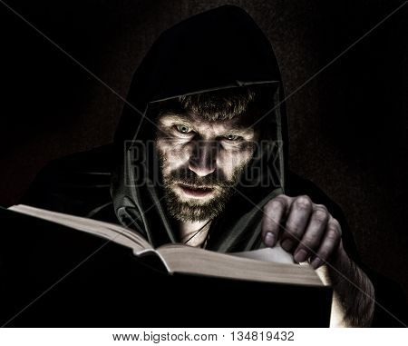 necromancer casts spells from thick ancient book by candlelight on a dark background.