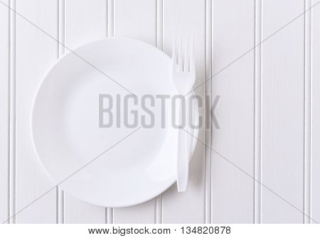 Top view of a white plate and white plastic fork on a white beadboard surface. Horizontal format with copy space.