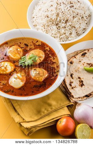 egg curry with roti/chapati and jeera rice, tasty and spicy anda curry with roti and rice, indian egg masala curry served in ceramic bowl with roti, salad and jeera rice