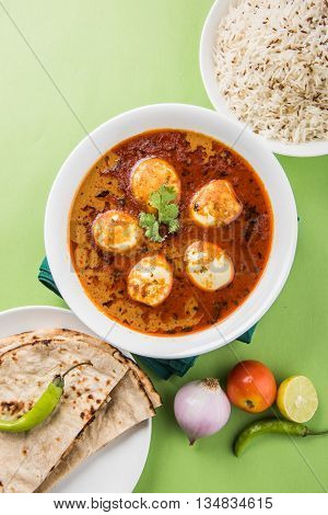 egg curry with roti/chapati and jeera rice, tasty and spicy anda curry with roti and rice, indian egg masala curry served in ceramic bowl with roti, salad and jeera rice