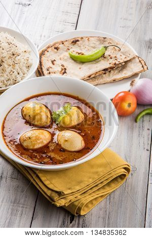 egg curry with roti/chapati and jeera rice, tasty and spicy anda curry with roti and rice, indian egg masala curry served in ceramic bowl with roti, salad and jeera rice