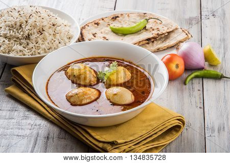 egg curry with roti/chapati and jeera rice, tasty and spicy anda curry with roti and rice, indian egg masala curry served in ceramic bowl with roti, salad and jeera rice