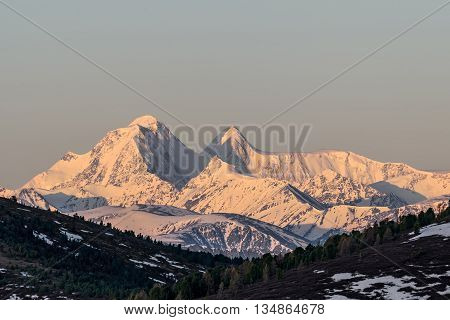 Scenic view with the beautiful mountain peaks with snow and glaciers slopes covered with snow and sparse brown vegetation and cedar trees at dawn