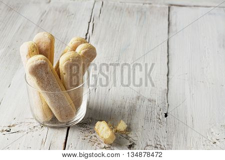 Sweet pastries, biscuits Savoiardi, ladies fingers in a glass mug on a light plain wooden background. selective focus
