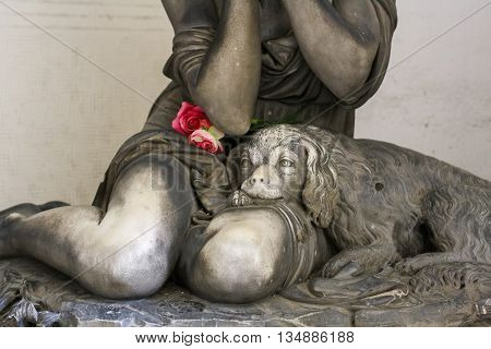 Statue of a dog on knees of grieving girl on monumental cemetery of Staglieno in Genoa.