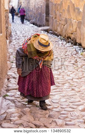 Unidentifiable Peruvian senior woman walking down cobblestone street