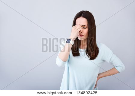 Unpleasant feelings. Cheerless sick woman feeling unhealthy and having a headache while standing isolated on white background