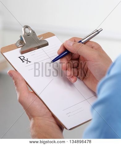 Male doctor writing prescription on clipboard. clinic