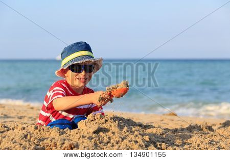 happy cute little boy play with sand on beach