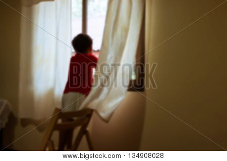 Blurry of little boy standing alone at window