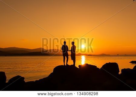 Couple love standing on the stone fishing at sea sunset backgroung