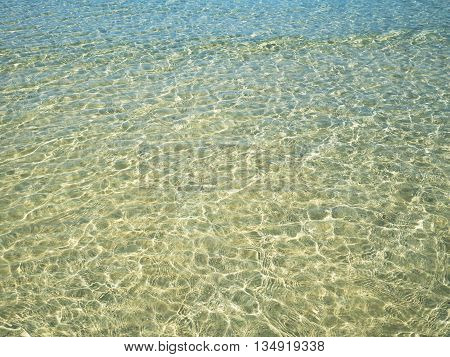 Background of transparent crystal green blue sea water surface ripple with sun reflection in summer. Water background. Ocean water texture.