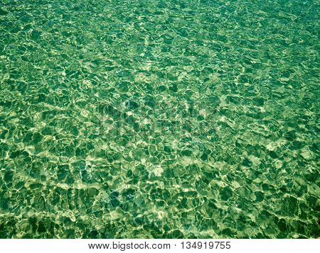 Background of transparent crystal green blue sea water surface ripple with sun reflection in summer. Water background. Ocean water texture.