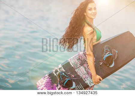 Young attractive brunette woman posing with wakeboard on the beach.
