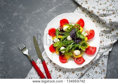 Fresh summer salad. Salad from tomatoes agaricus lettuce pepper and mozzarella. Grey beton background.
