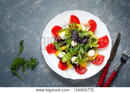 Fresh summer salad. Salad from tomatoes agaricus lettuce pepper and mozzarella. Grey beton background.