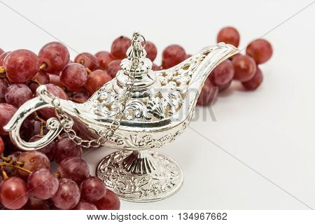 Silver Aladdin's magic lamp and red grapes. Ramadan Eid concept background