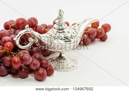 Silver Aladdin's magic lamp and red grapes. Ramadan Eid concept background