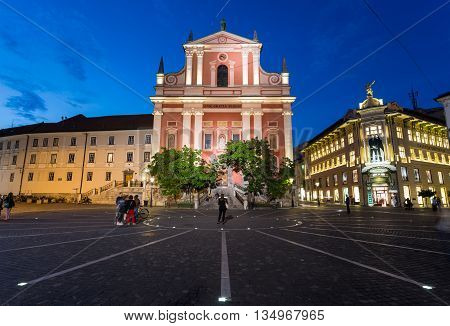 LJUBLJANA SLOVENIA - 26TH MAY 2016: The outside of Franciscan Church of the Annunciation and Preseren Square in Ljubljana at night. People can be seen.