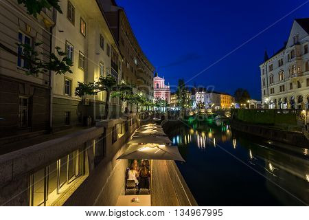 LJUBLJANA SLOVENIA - 26TH MAY 2016: A view along the Ljubljana canal towards the Franciscan Church of the Annunciation and Preseren Square at night. Other buildings and people can be seen.