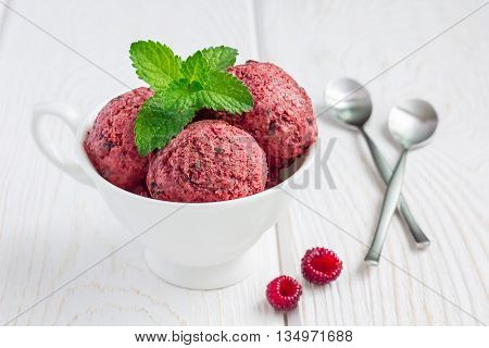 Homemade raspberry yogurt chocolate chips ice cream balls in cup on a white wooden table horizontal