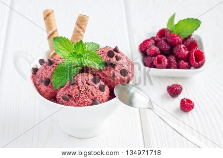 Homemade raspberry yogurt chocolate chips ice cream balls in cup on a white wooden table horizontal