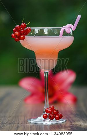 Glass of cold pink cocktail with straw on green background bokeh