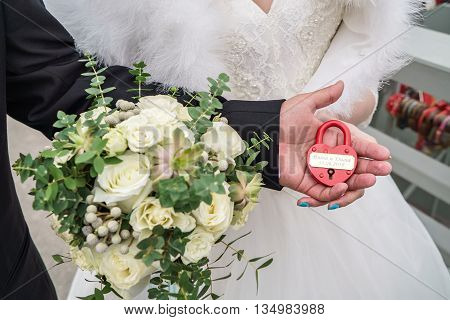 Red wedding lock with the words of Vita and Dima 30.04.2016 in the hands of the bride and groom. Wedding theme, symbol of love, newlyweds