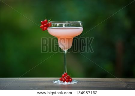 Glass of cold pink cocktail on green background bokeh