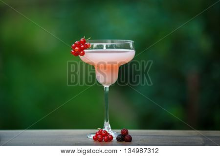 Glass of cold pink cocktail on green background bokeh