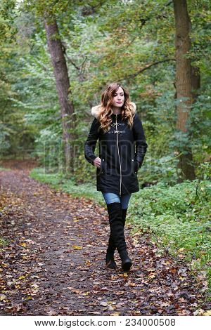 Young Woman Wearing Winter Coat And Overknee Boots On Solitary Forest Walk In Autumn
