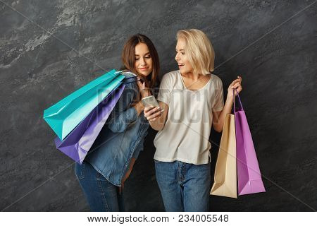 Happy Casual Girlfriends With Shopping Bags. Two Excited Shopaholics Posing With Purchases And Using