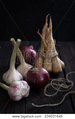 Onions, Garlic And Parsley On A Dark Wooden Table