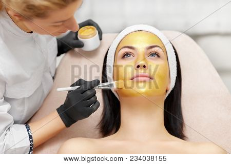 Applying Of Gold Facial Mask On Skin Of Beautiful Brunette.