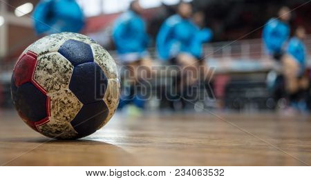 Handball ball on court's floor. Blurred court and exercising team background. Space for text.