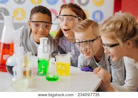 Fond Of Chemistry. The Group Of Upbeat Teenage Students Being Gathered Around The Table In Their Sch