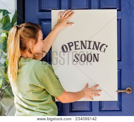 Woman putting on store opening soon sign