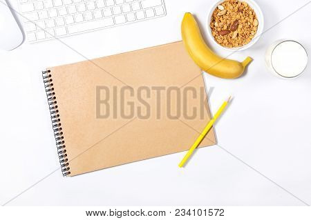 White Keyboard, Mouse, Scetchbook; Yellow Pencils, Plate With Granola, Banana And Glass Of Milk On W