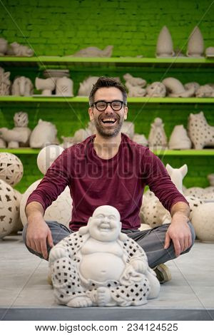 Portrait of Smiling Young Ceramist in the Bright Modern Ceramic Workshop Sitting Next to his Sculpture. Small Business Concept.