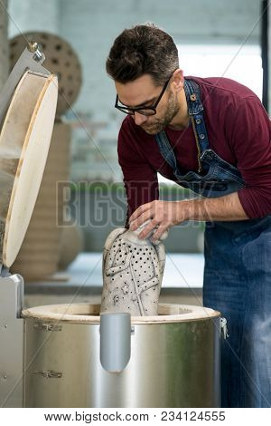 Ceramist Dressed in an Apron Placing Clay Sculpture in the Electric Oven.